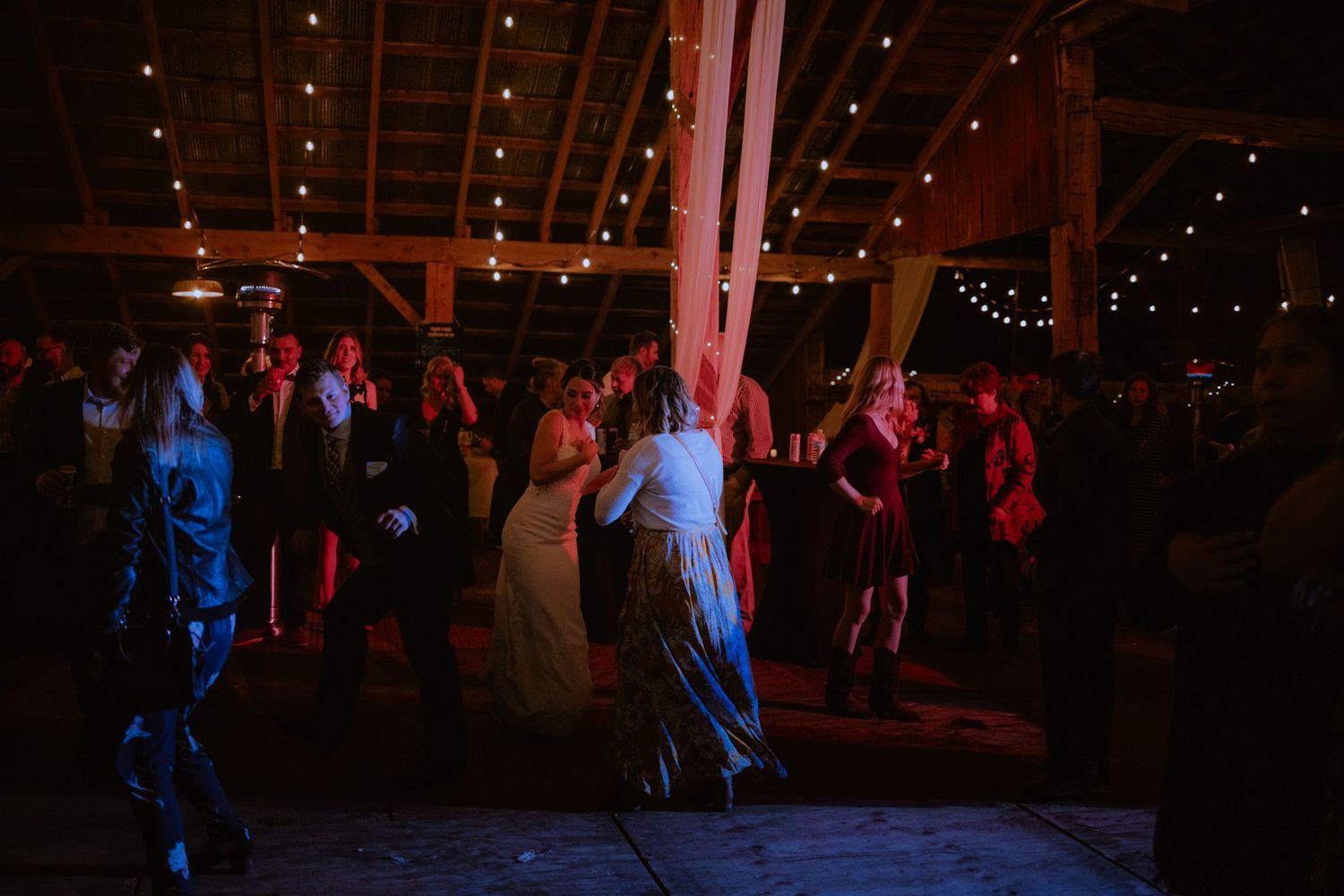 an image of wedding guests dancing in a barn lit with DJ lighting