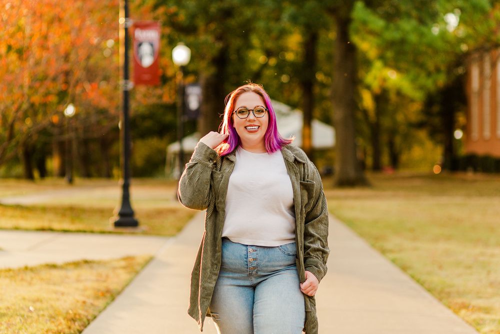 Autumn campus scene with graduate walking along tree-lined path in casual attire.