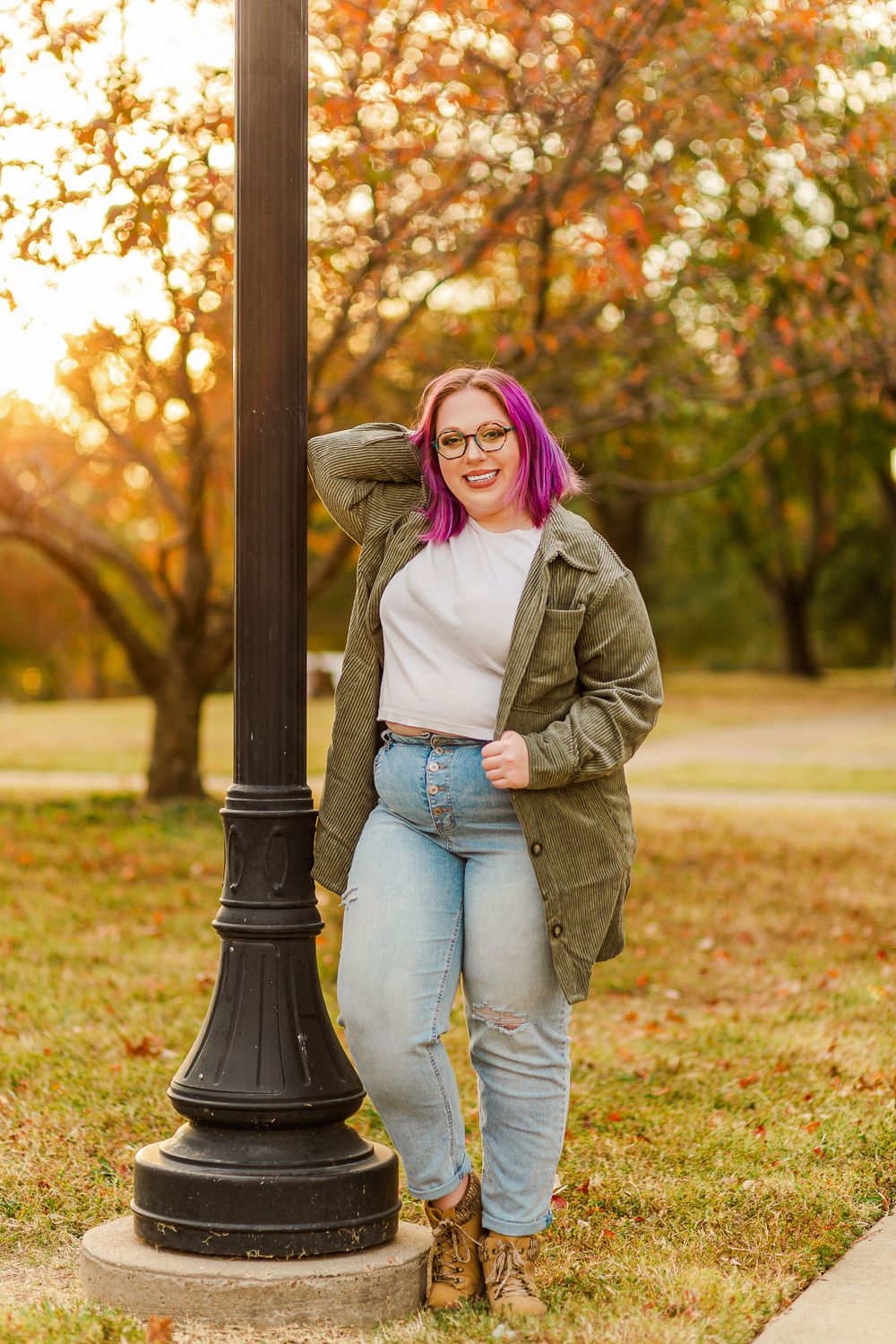 Casual fall fashion with pink hair, olive jacket and light denim against autumn foliage background.