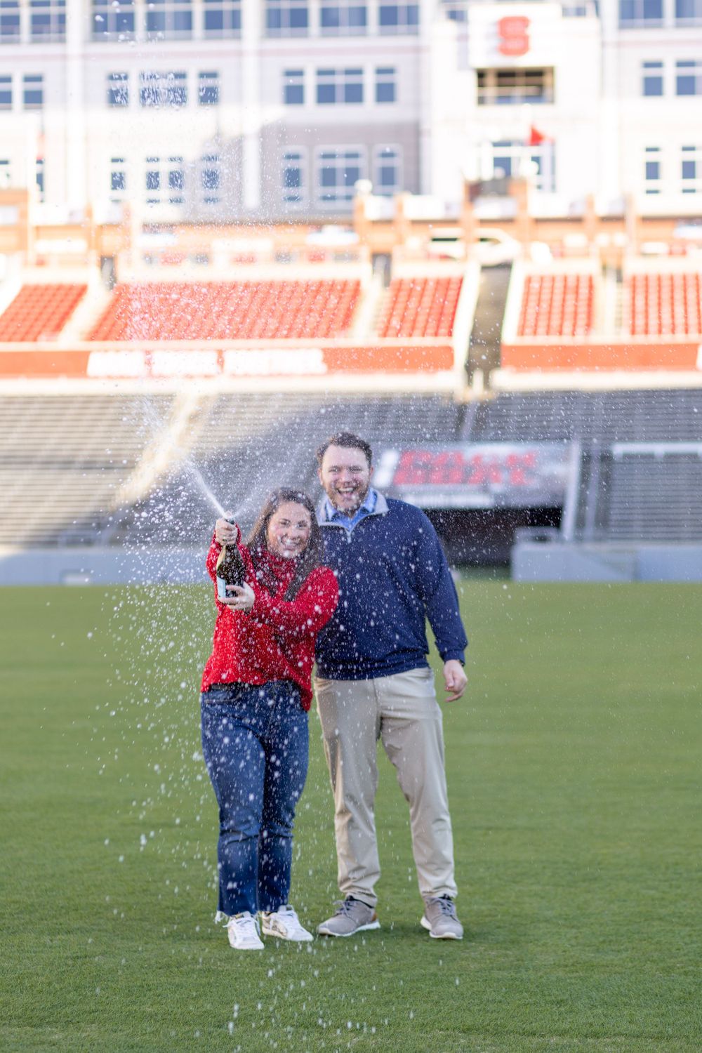 A couple pops a bottle of champagne at their NC State Proposal Photo Session.