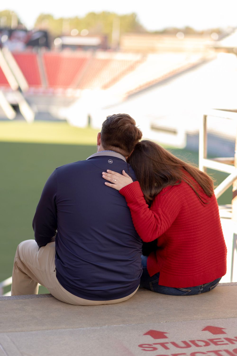 A newly engaged couple sits overlooking the NC State football stadium.