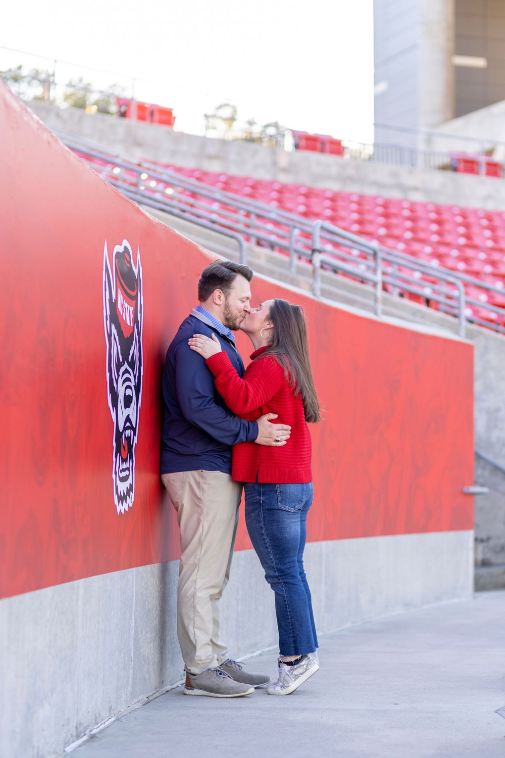 A couple posed against an NC State background at their engagement photoshoot at Carter Finley Stadium.