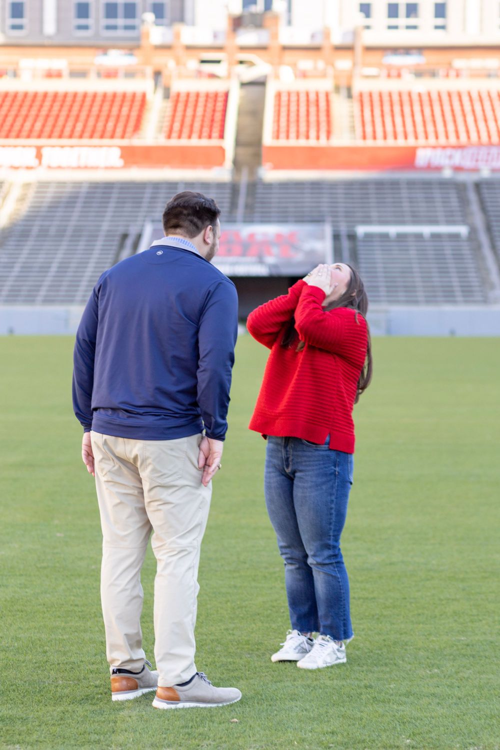 A women in a red sweater covers her face with her hands as she reacts to finding out about her engagement party.