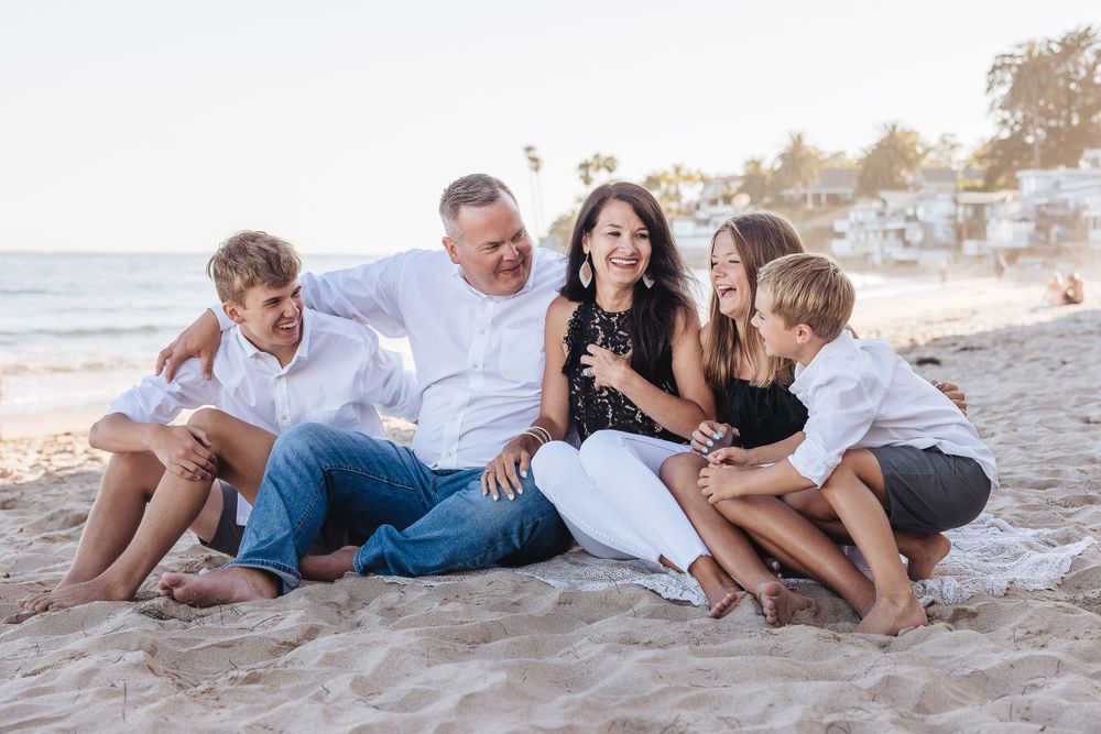 Family sharing laughs while sitting together on beach during sunset.