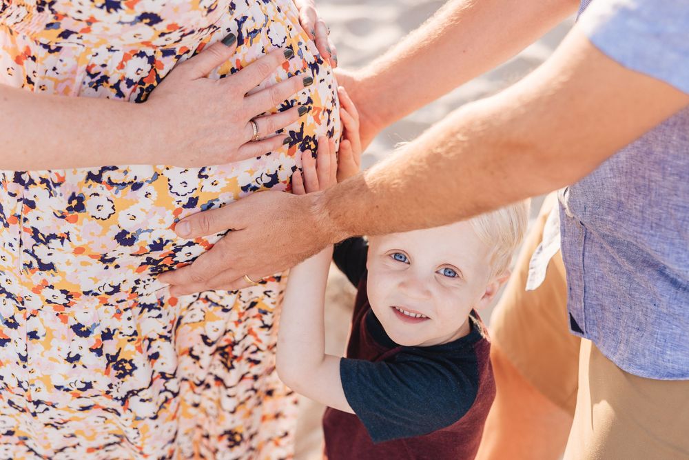 A small child in a navy outfit reaches up during a beach photoshoot.