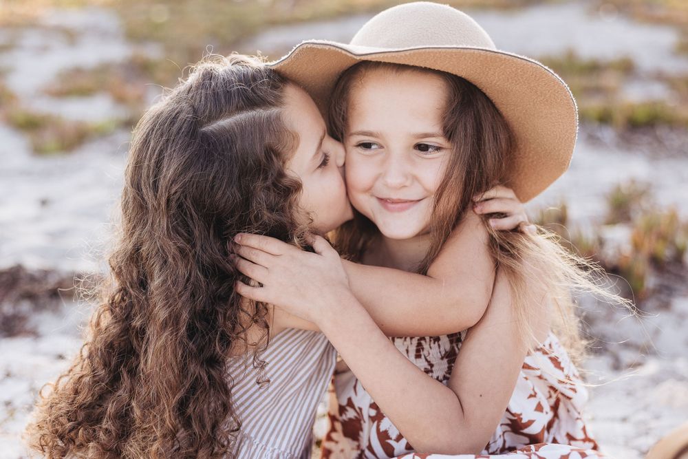 Two children sharing sweet moment with hat on beach.