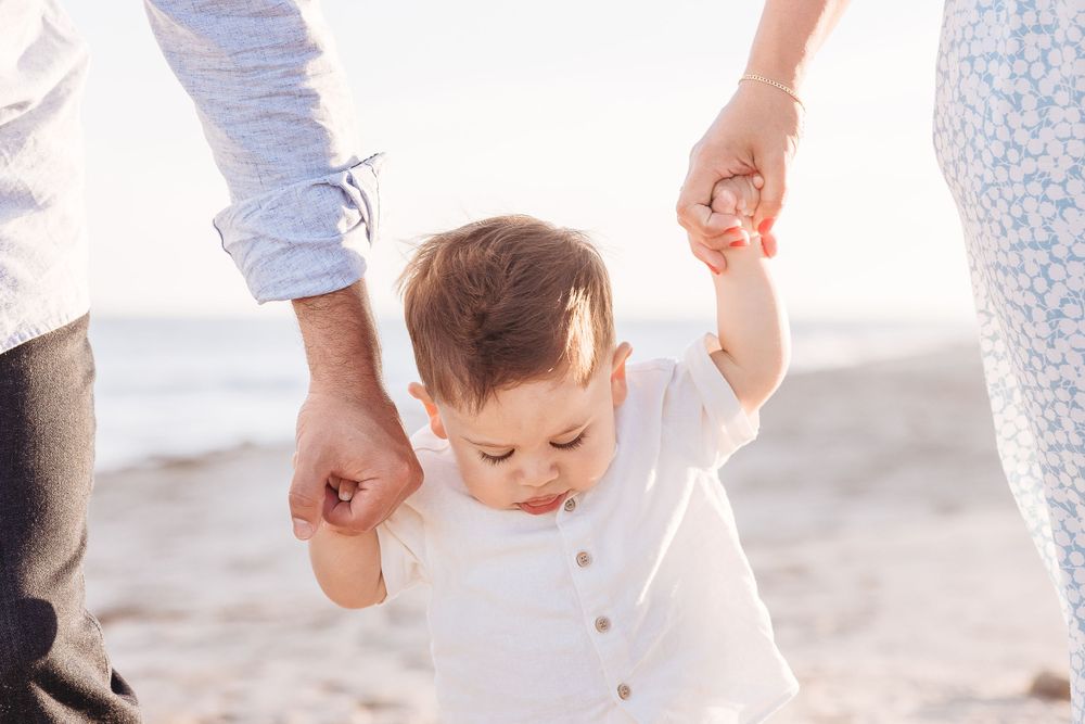 Small child taking first steps while holding hands on beach.