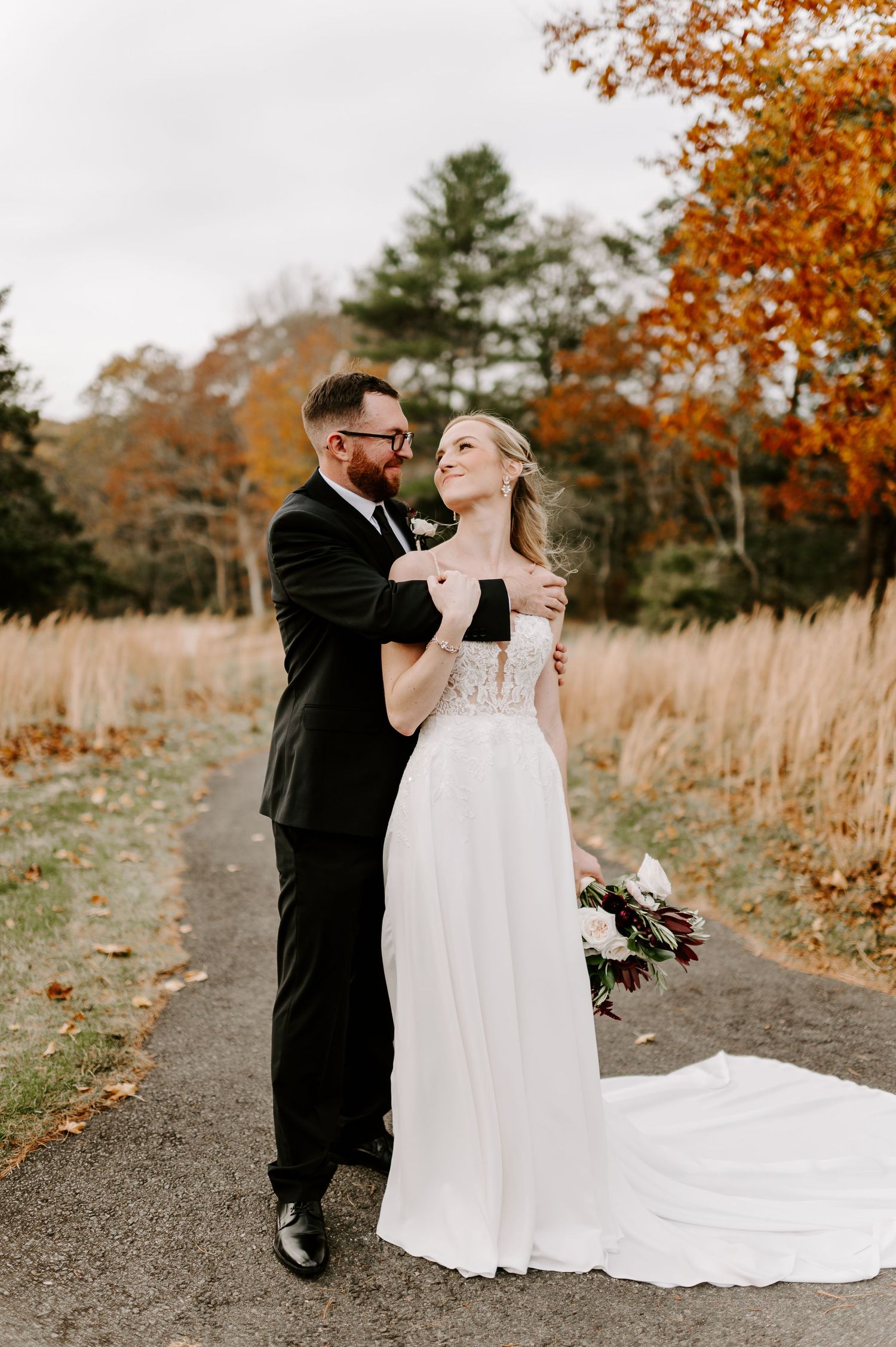 A romantic autumn wedding photo shoot with fall foliage and a flowing white dress on a path.