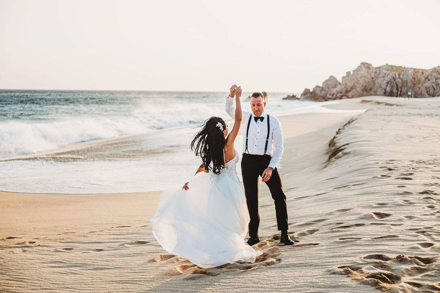 Husband twirling wife on the beaches of Cabo after their wedding.