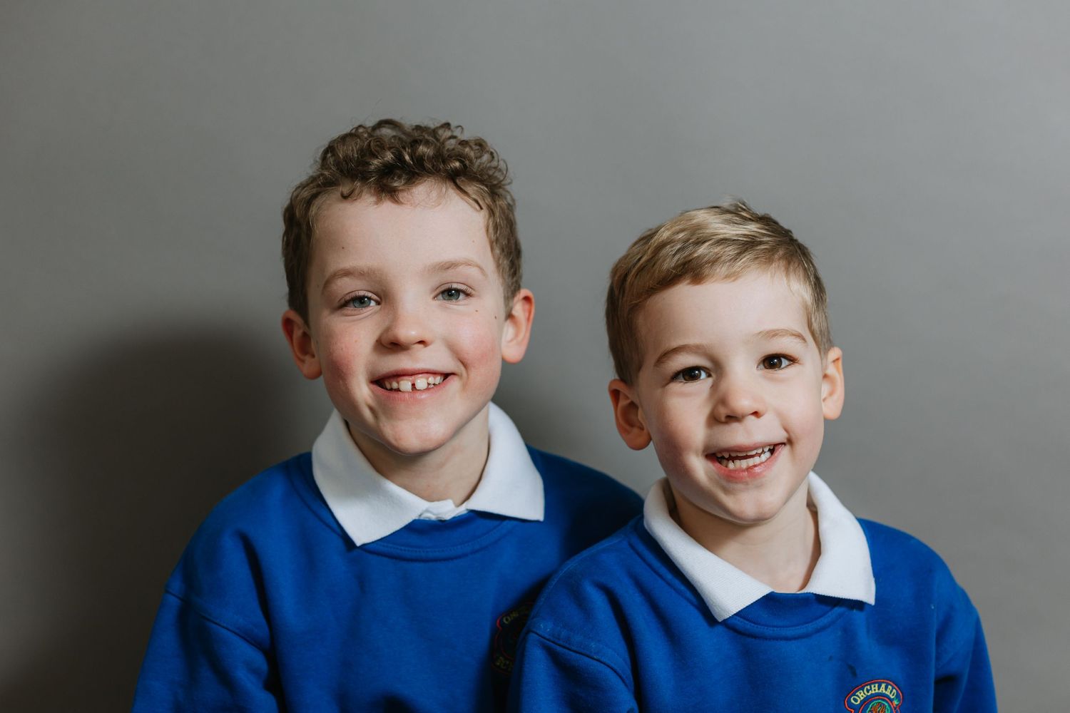 Two students in matching bright blue school uniforms smile at the camera during picture day.