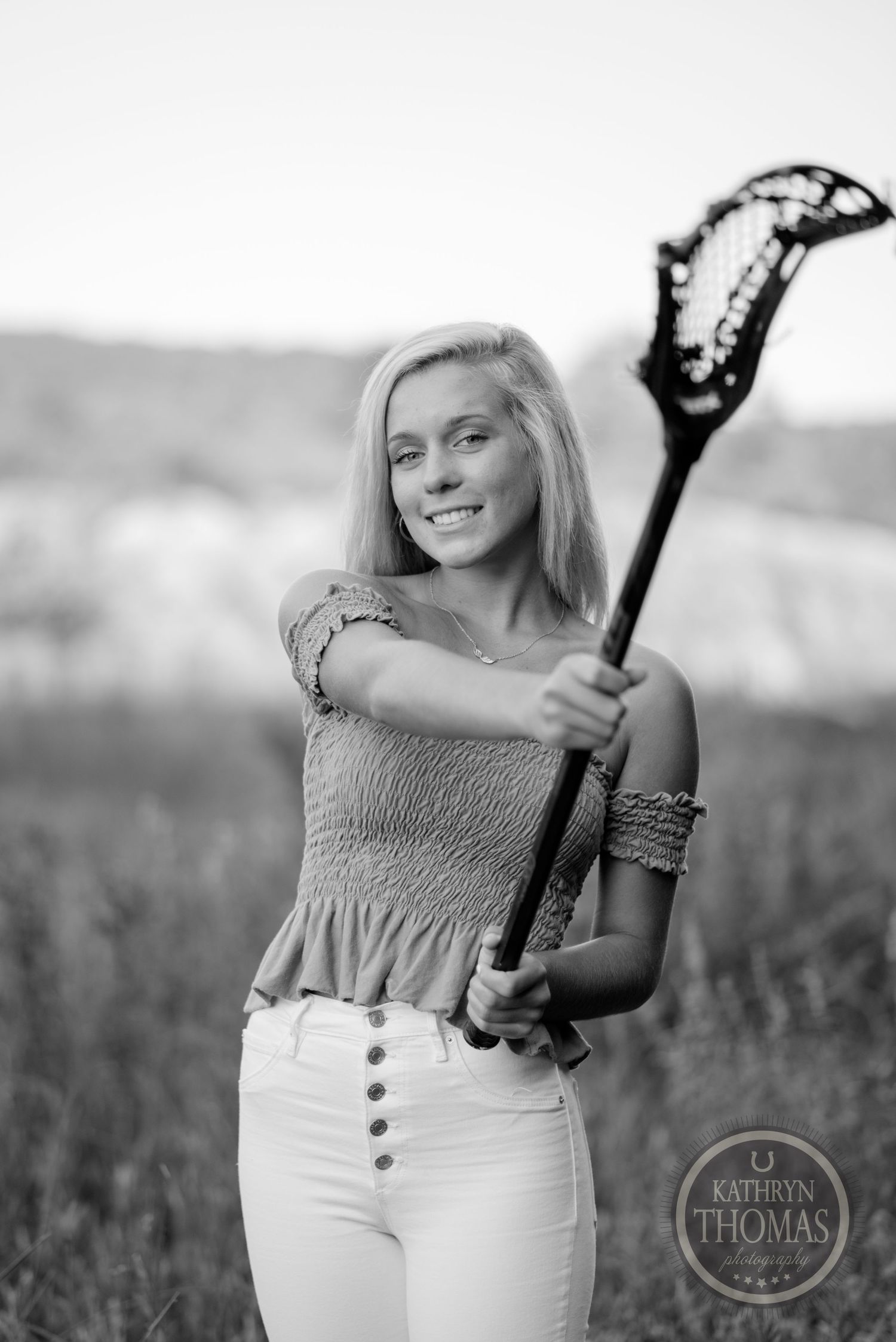 Black and white portrait with a lacrosse stick against a natural outdoor background.