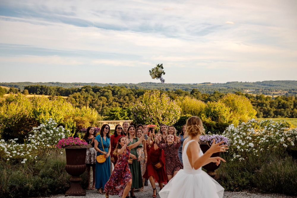 Wedding bouquet toss at sunset with guests gathered on a hilltop overlooking a scenic landscape.
