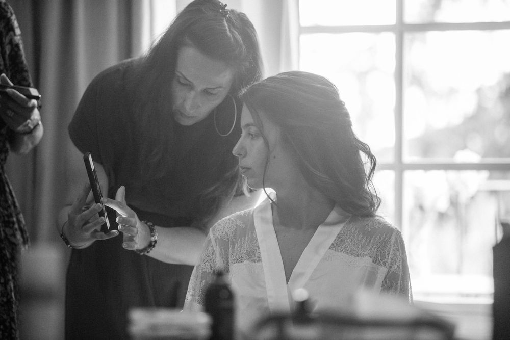 Black and white photo of bridal preparation with styling taking place near a window.
