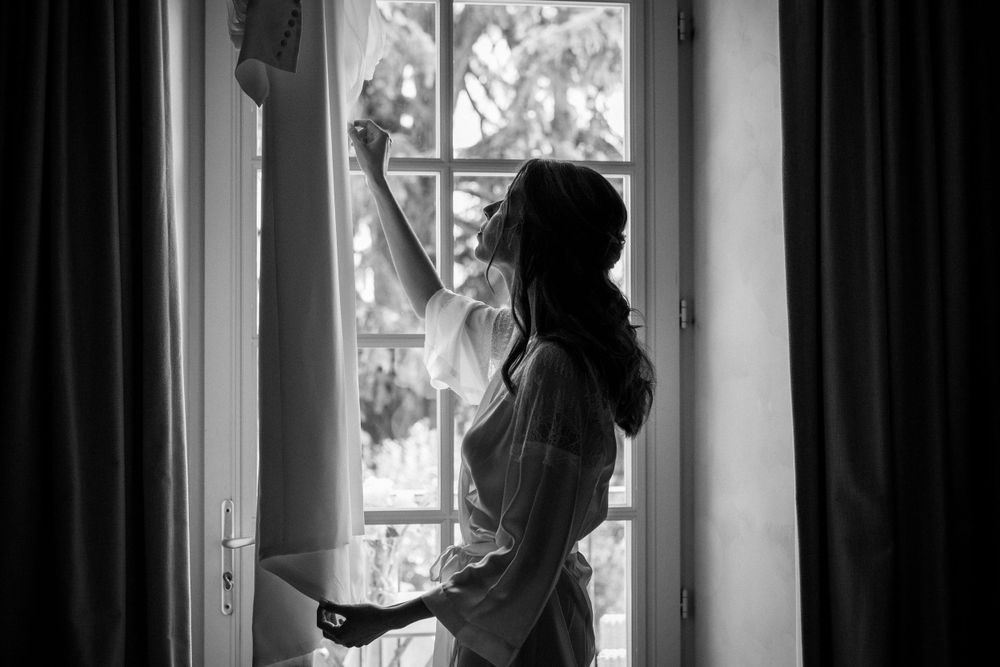 Silhouette of bride in morning light stretching by window in black and white.