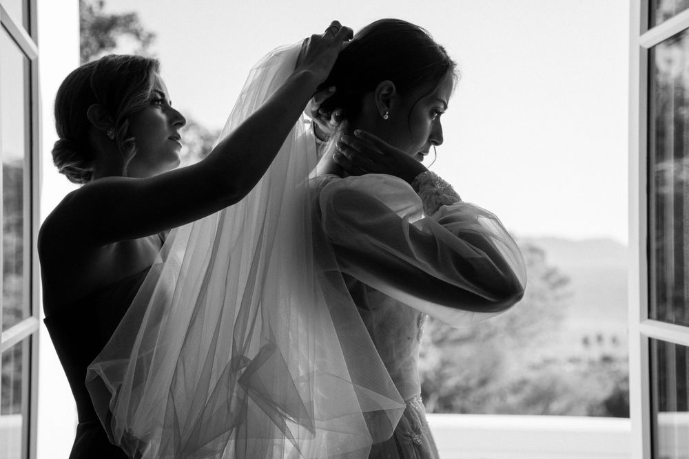 Black and white image of wedding veil being adjusted near a bright window.