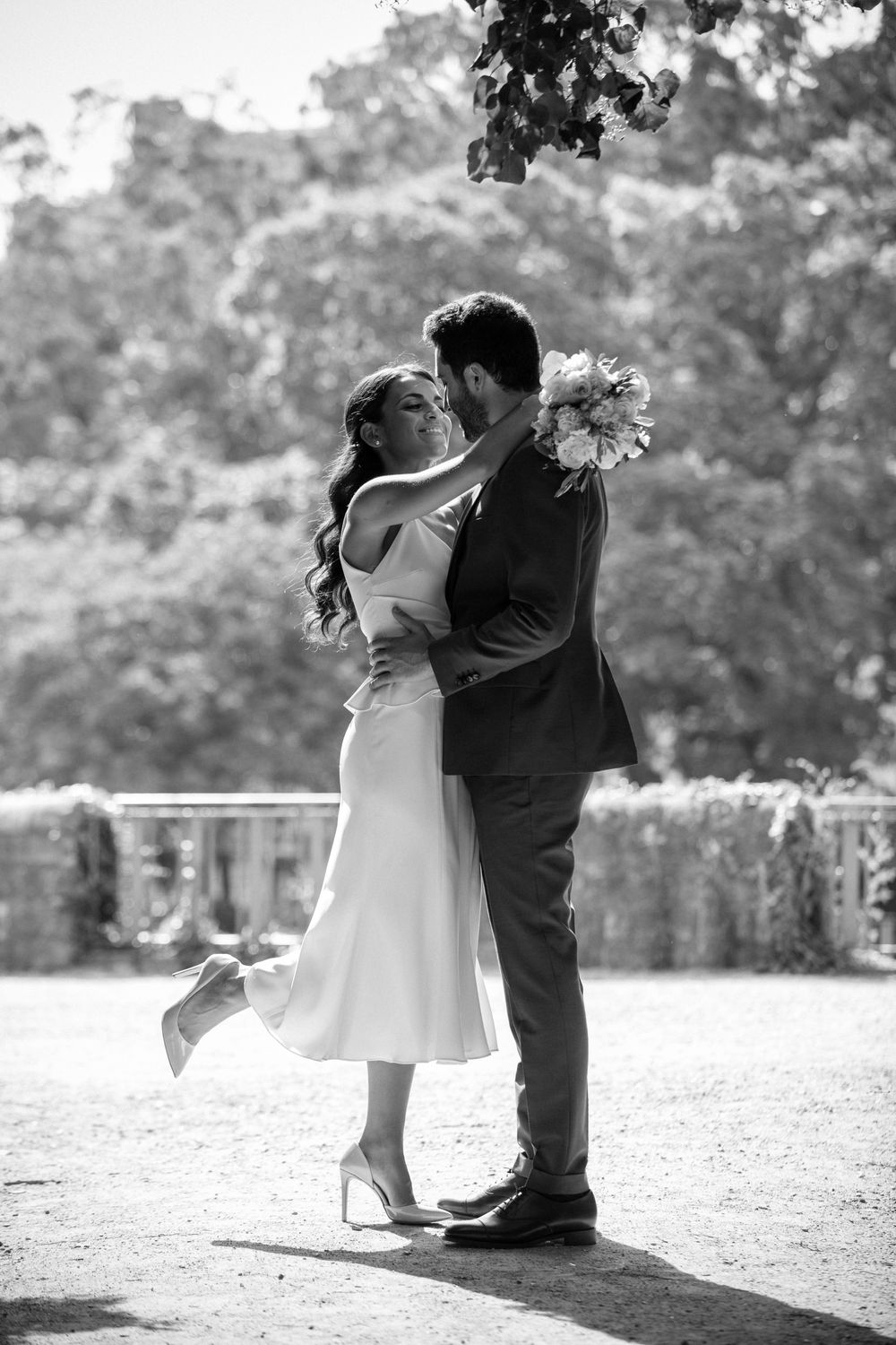 A romantic black and white wedding photo of a couple embracing outdoors with the bride's foot lifted.