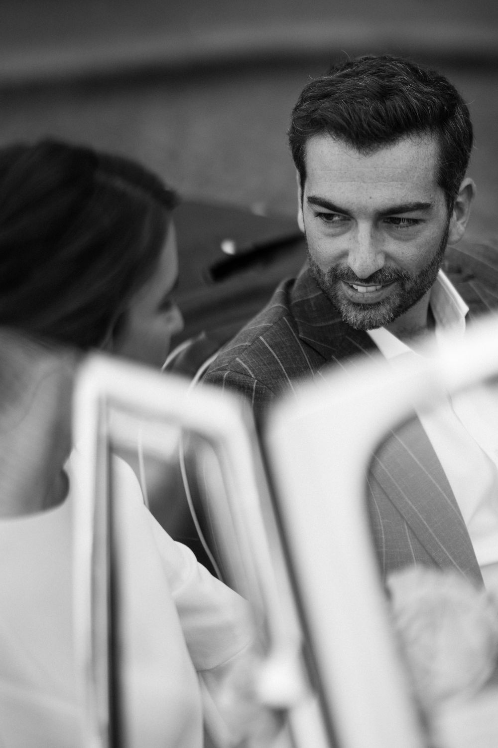 Black and white candid moment showing tender interaction between couple near car.