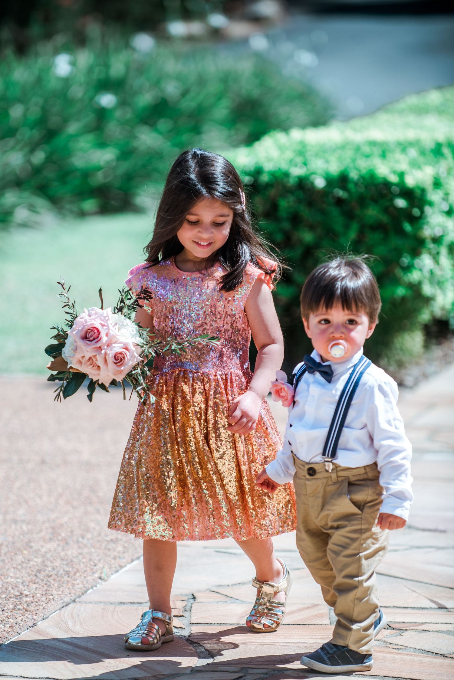 Young wedding attendants walking together in formal attire on stone path.