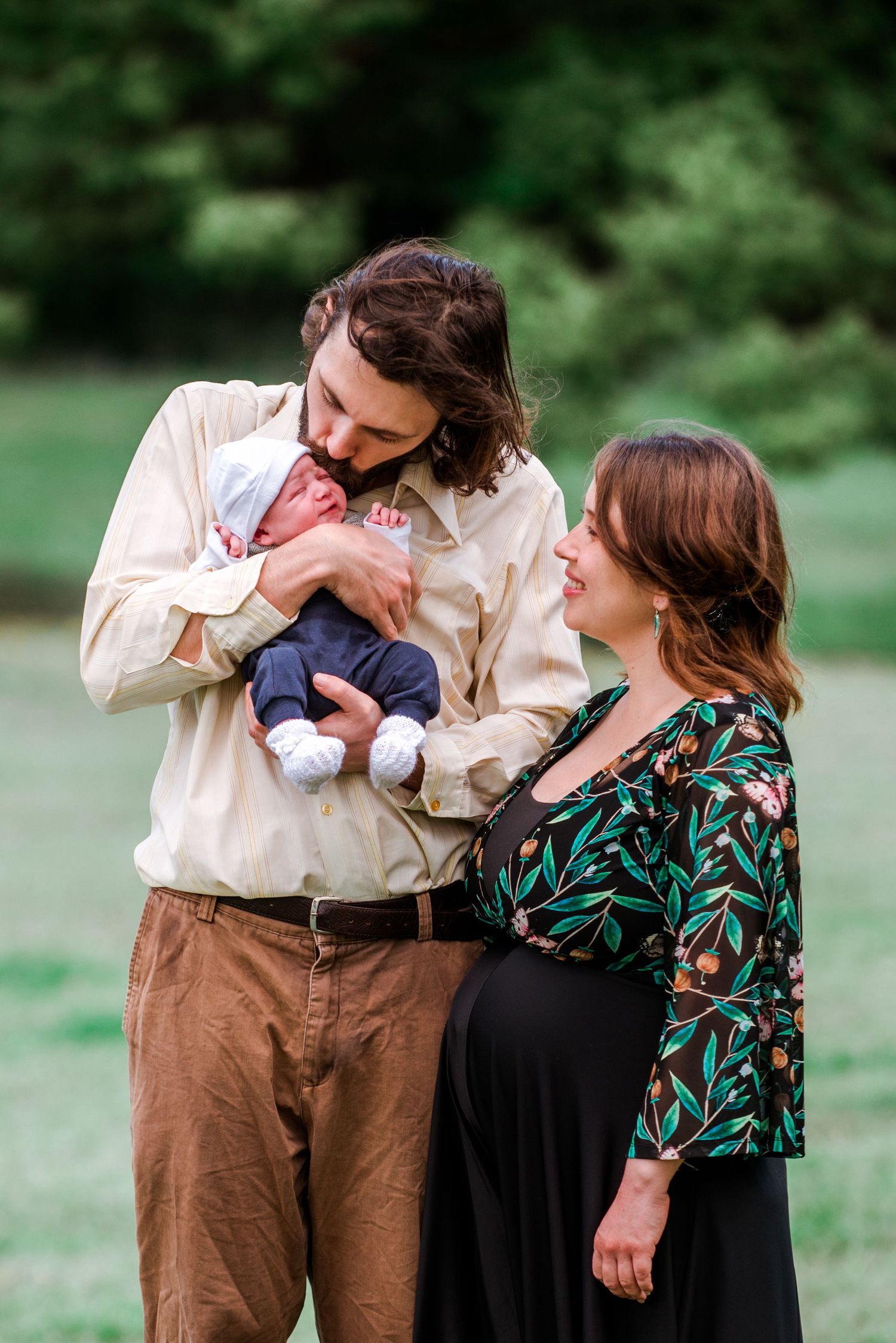 Couple admires their newborn baby while standing in a sunny meadow.