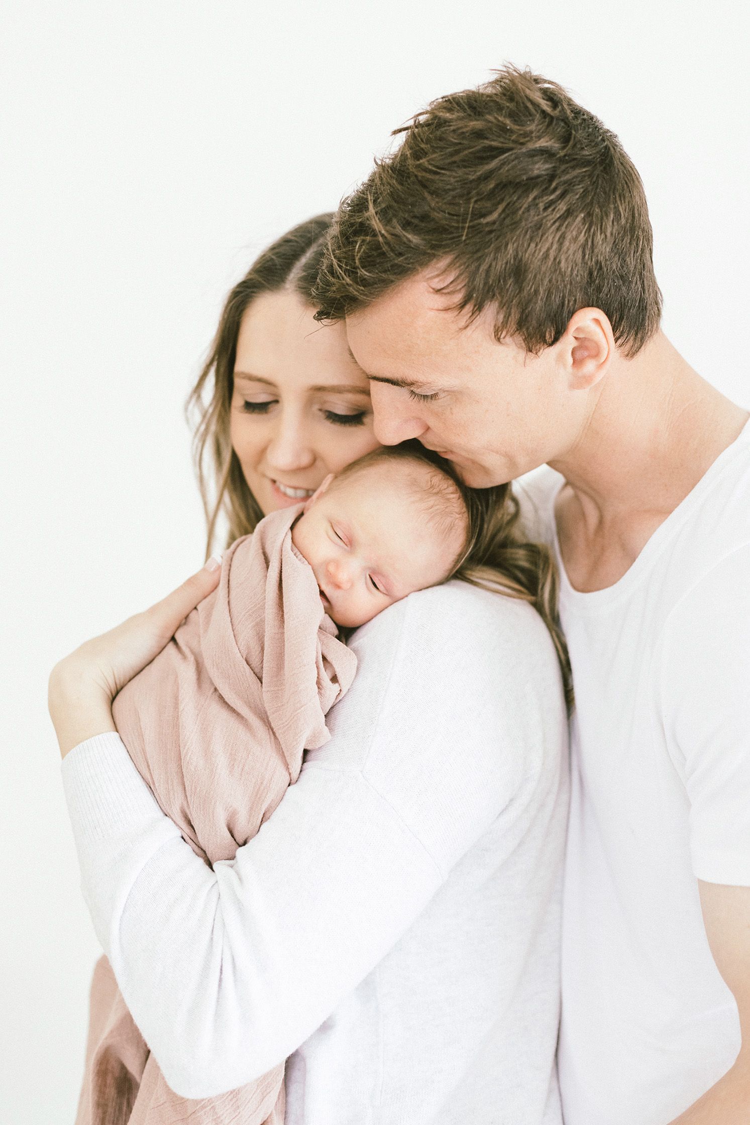 Intimate family moment captured in white studio setting showing affection.