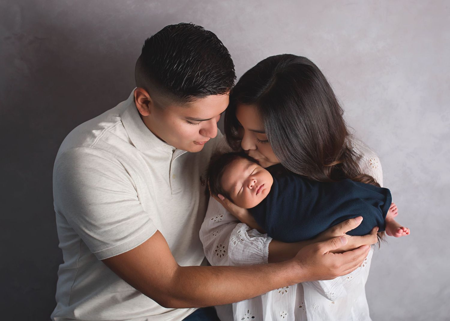 Intimate family portrait in white and navy against grey background.