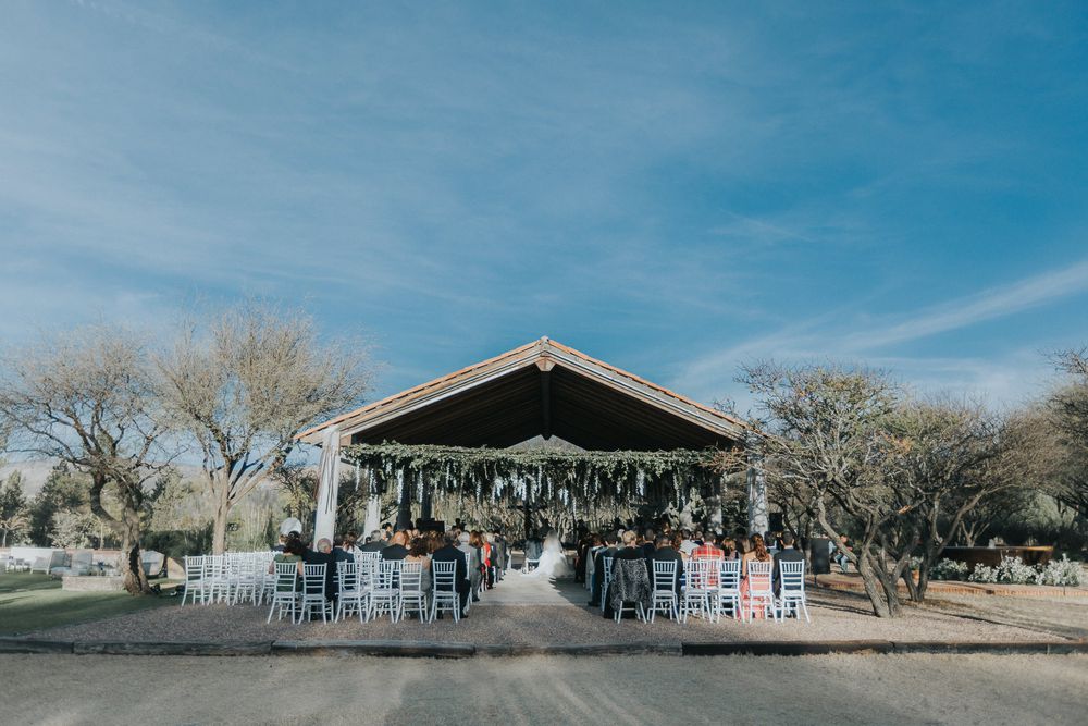 An outdoor wedding ceremony setup under a rustic wooden pavilion against blue skies.