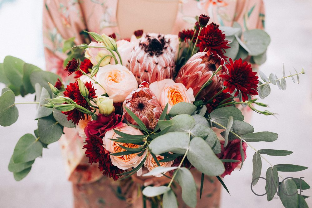 Romantic bridal bouquet featuring burgundy and peach flowers with eucalyptus accents.