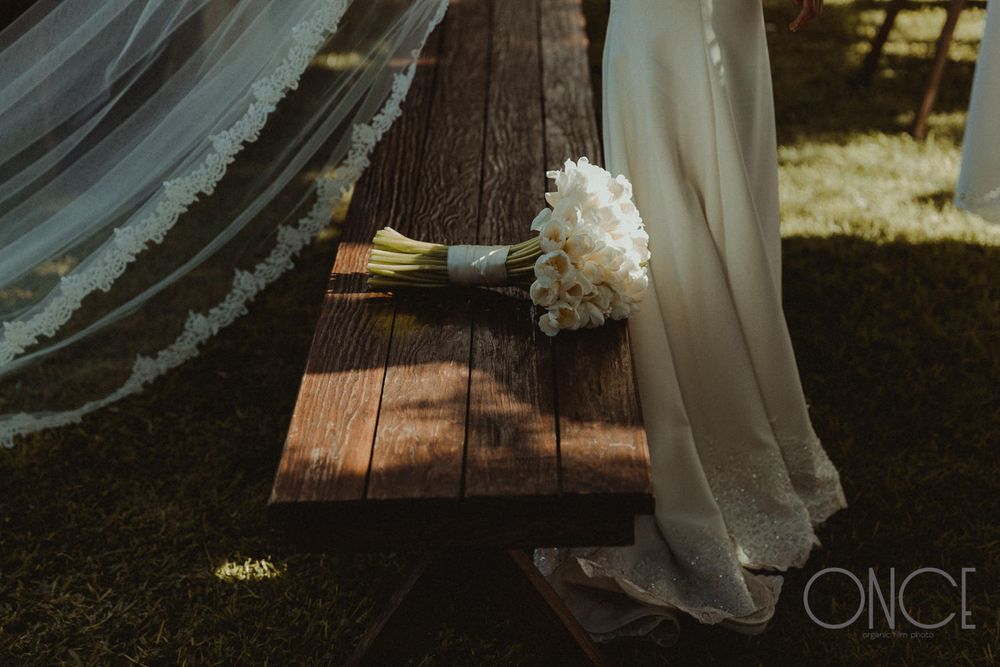 Classic white bridal bouquet and veil resting on a wooden bench in natural lighting.