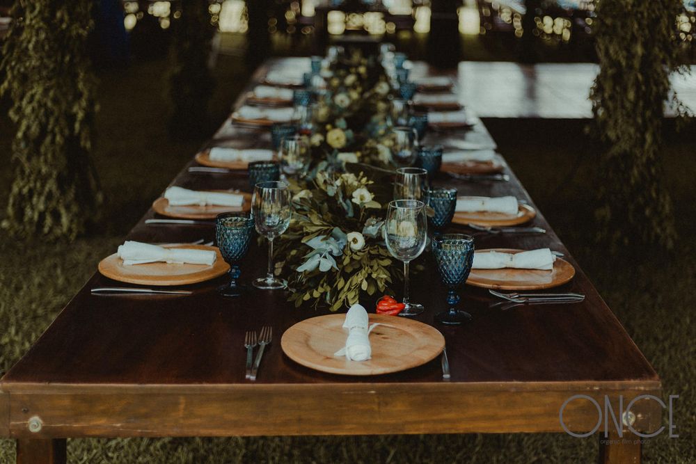Moody table setting with blue glassware and greenery garland runner on wooden farmhouse table.