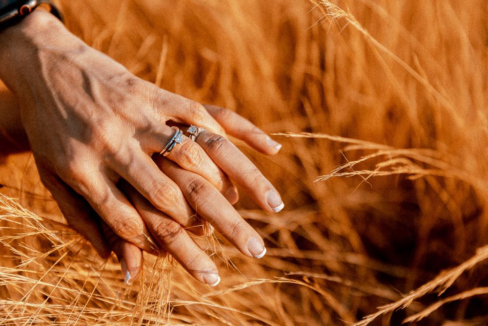 A close-up of a manicured hand with engagement ring against golden wheat stalks.
