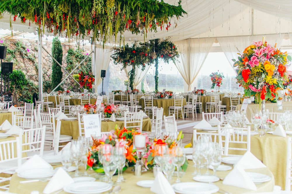 An elegant wedding reception setup with white chairs and vibrant floral centerpieces under a draped tent ceiling.
