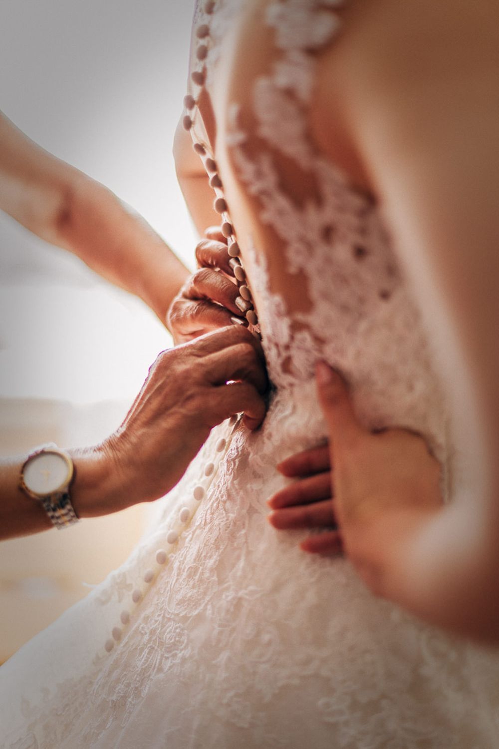Close-up detail shot of delicate lace buttons on a wedding dress being fastened.