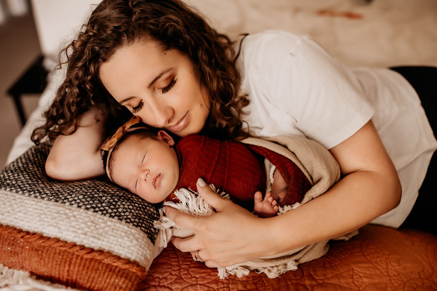 A mother and her newborn baby snuggle on the bed.
