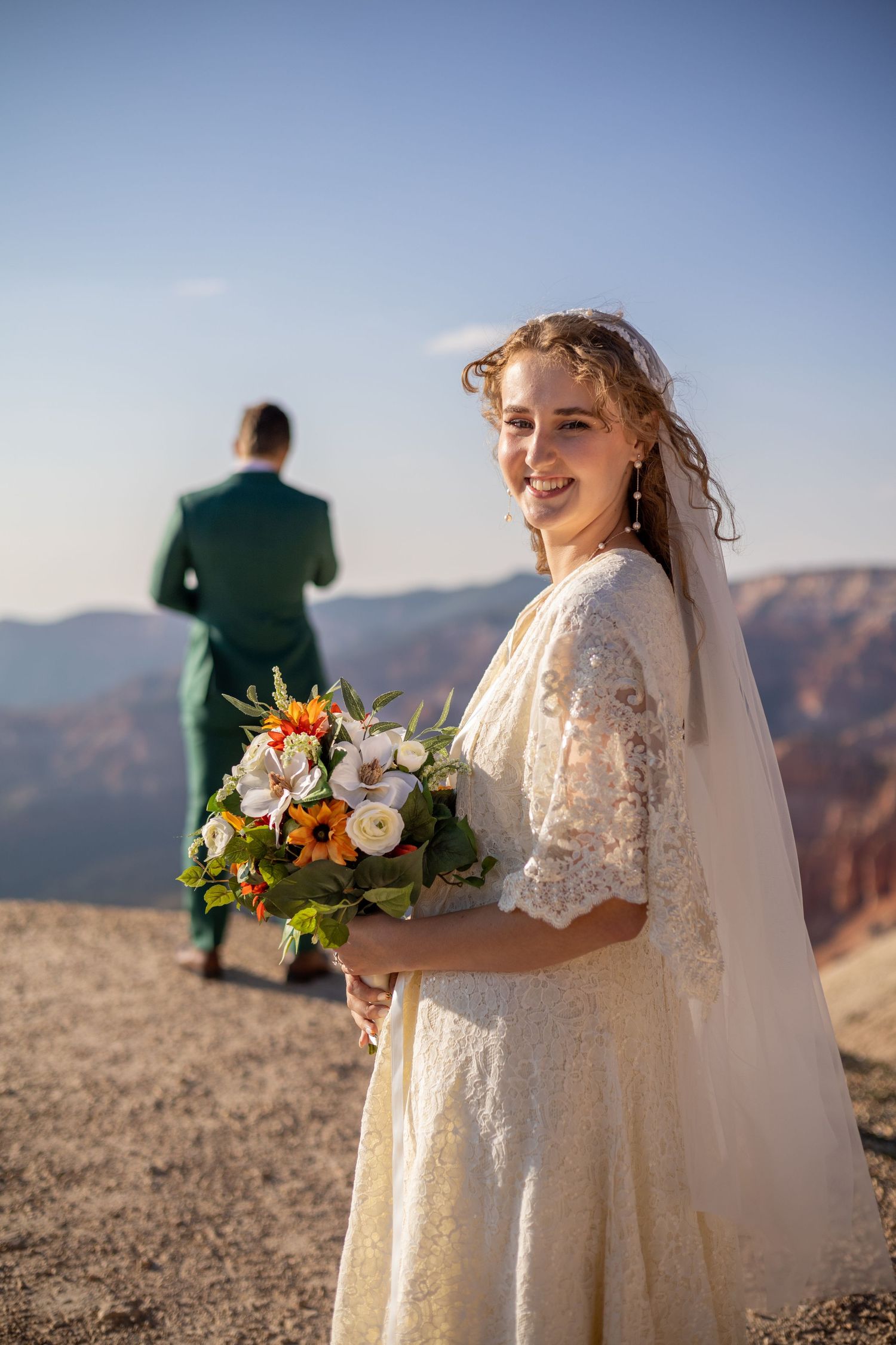 Bride holding autumn-colored bouquet against mountainous backdrop.