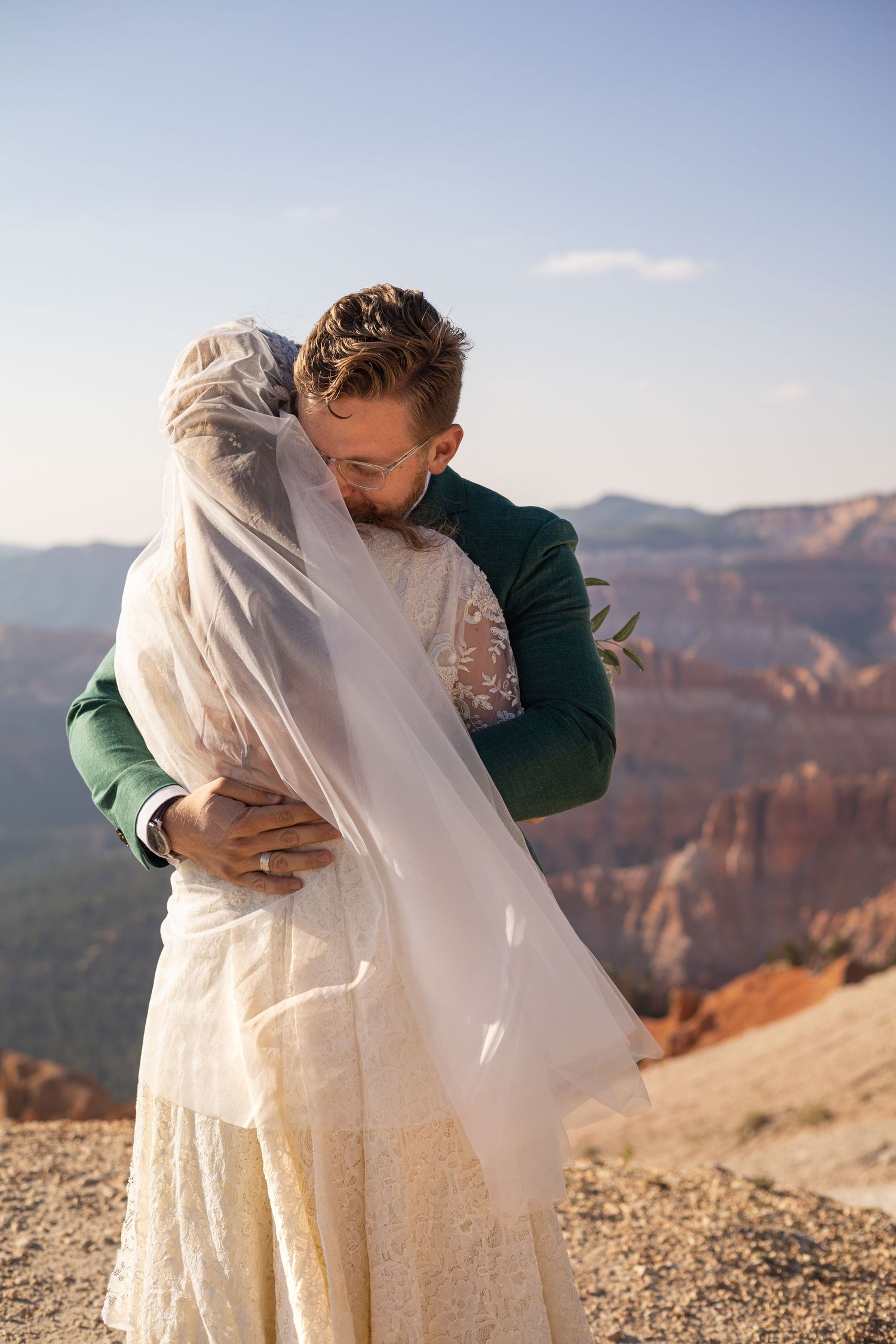 A romantic wedding couple embraces against the backdrop of a majestic canyon landscape at sunset.