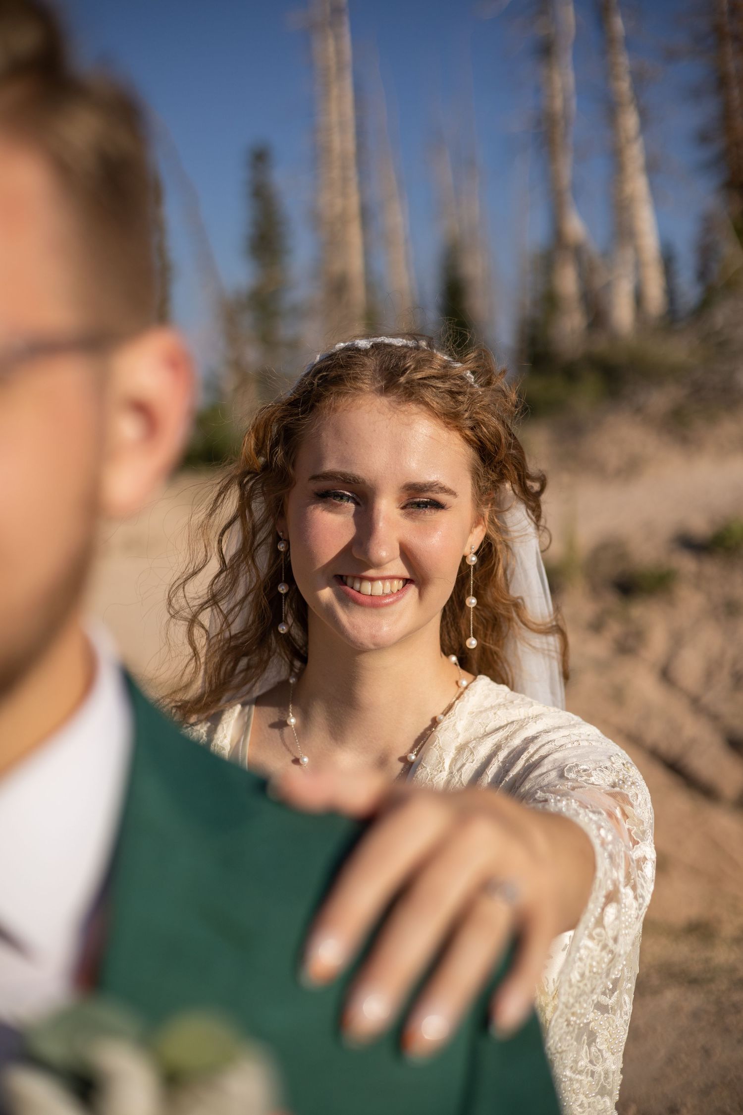 Close-up wedding portrait against mountain backdrop with sunlit pine trees.