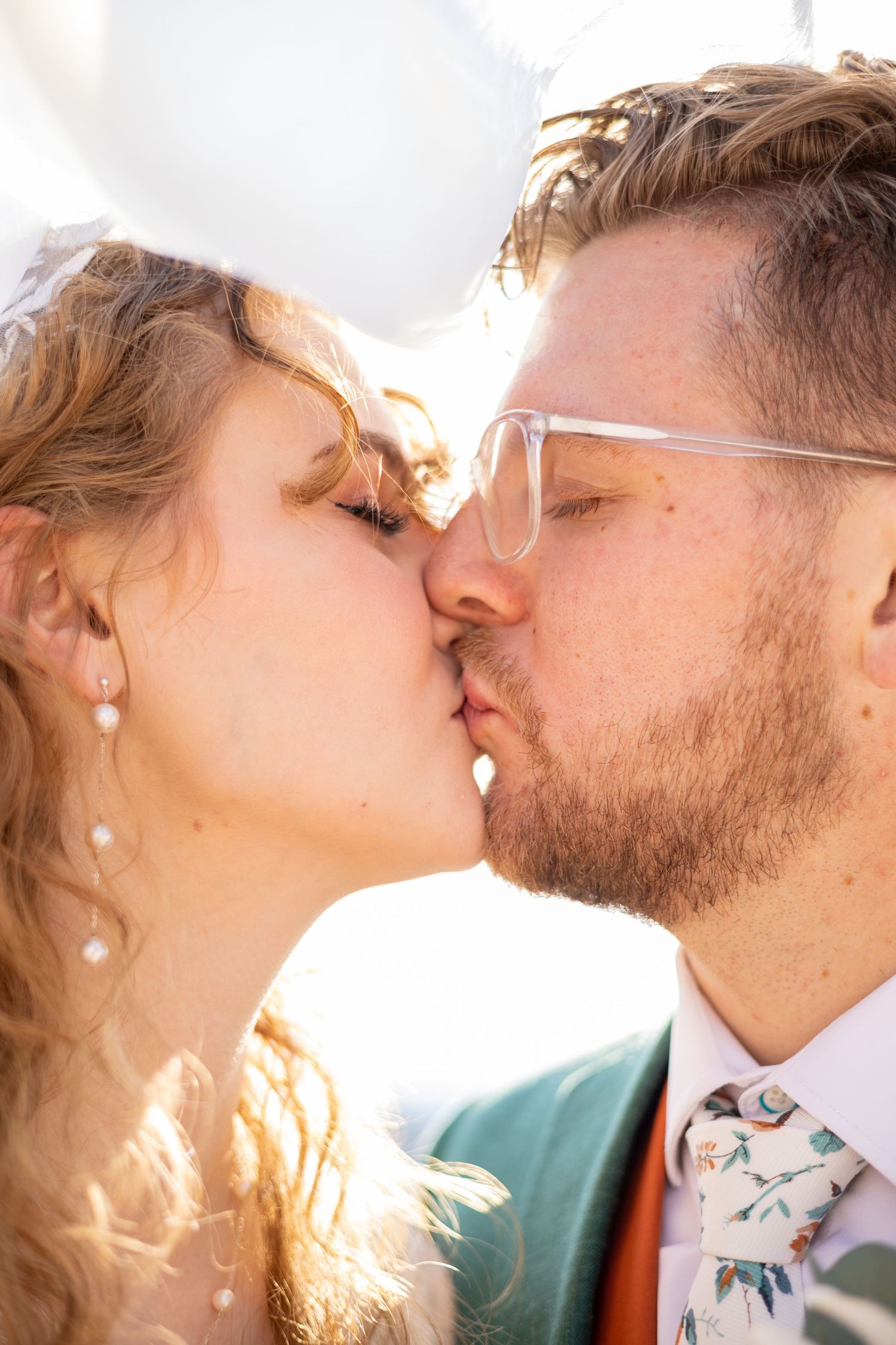 Close-up of a tender kiss between newlyweds with sunlight creating a romantic glow.