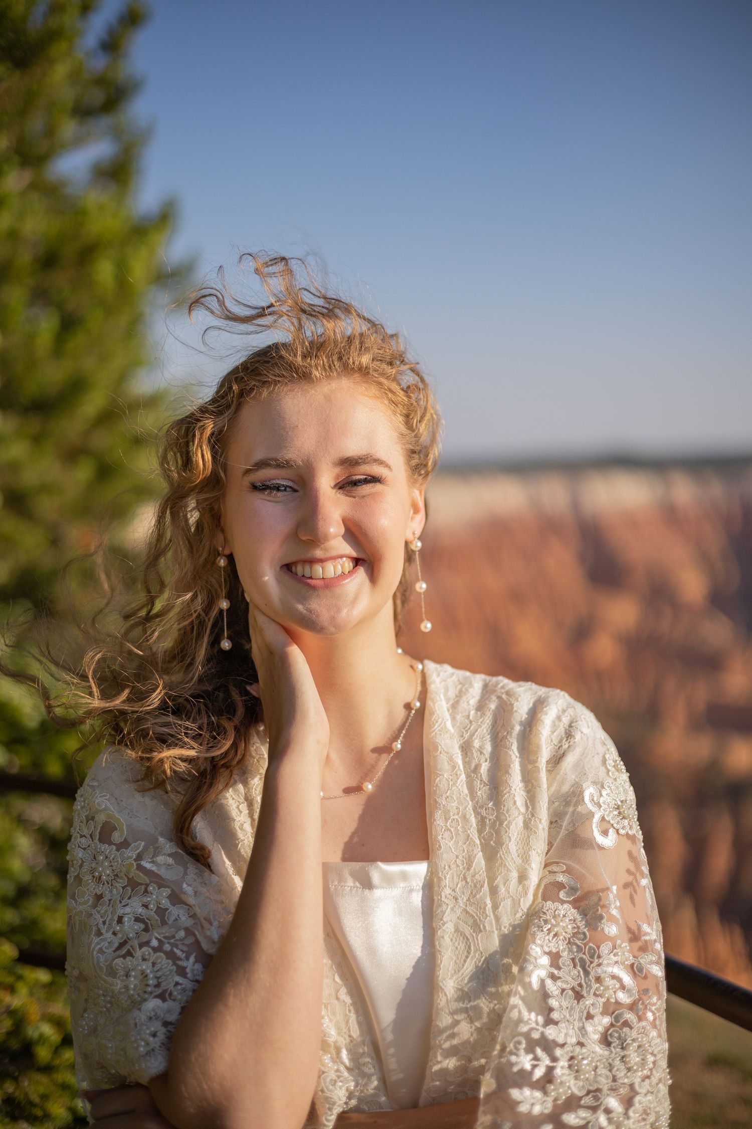 Bride in lace dress smiles joyfully against a scenic canyon backdrop.