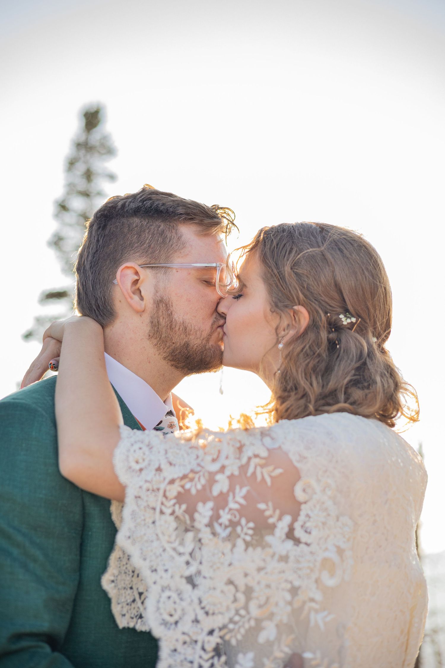 A couple shares a tender kiss during sunset with soft backlighting.