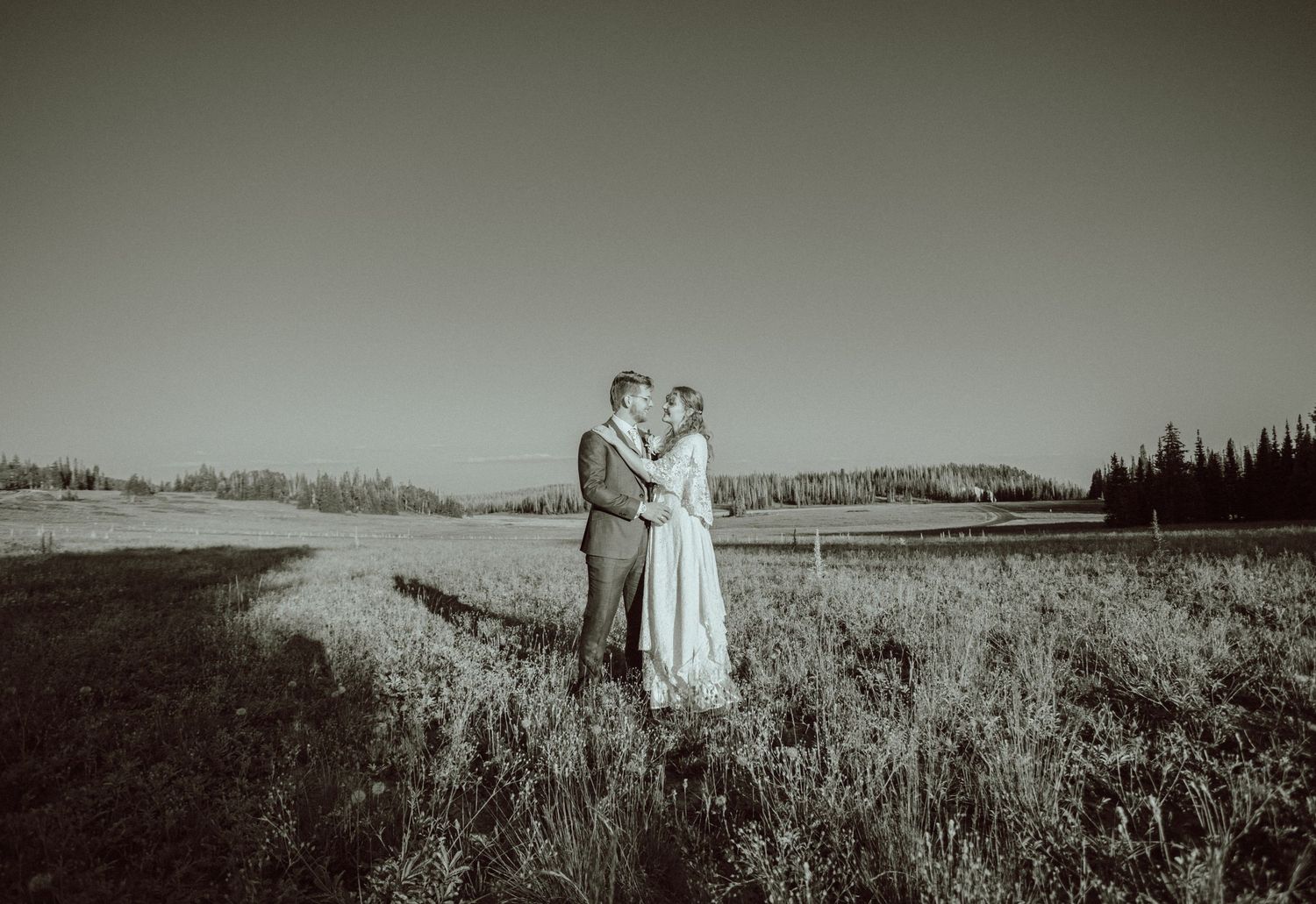 A romantic black and white panoramic shot of a couple in a vast meadow.