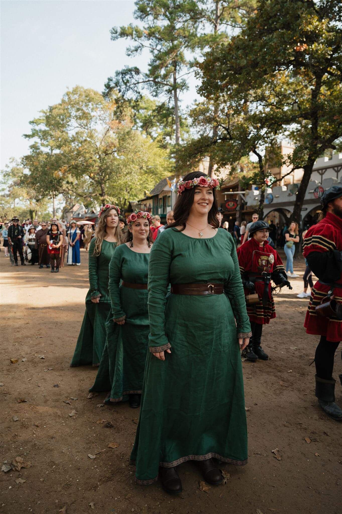 Women in emerald green medieval dresses walk in formation at a renaissance festival.