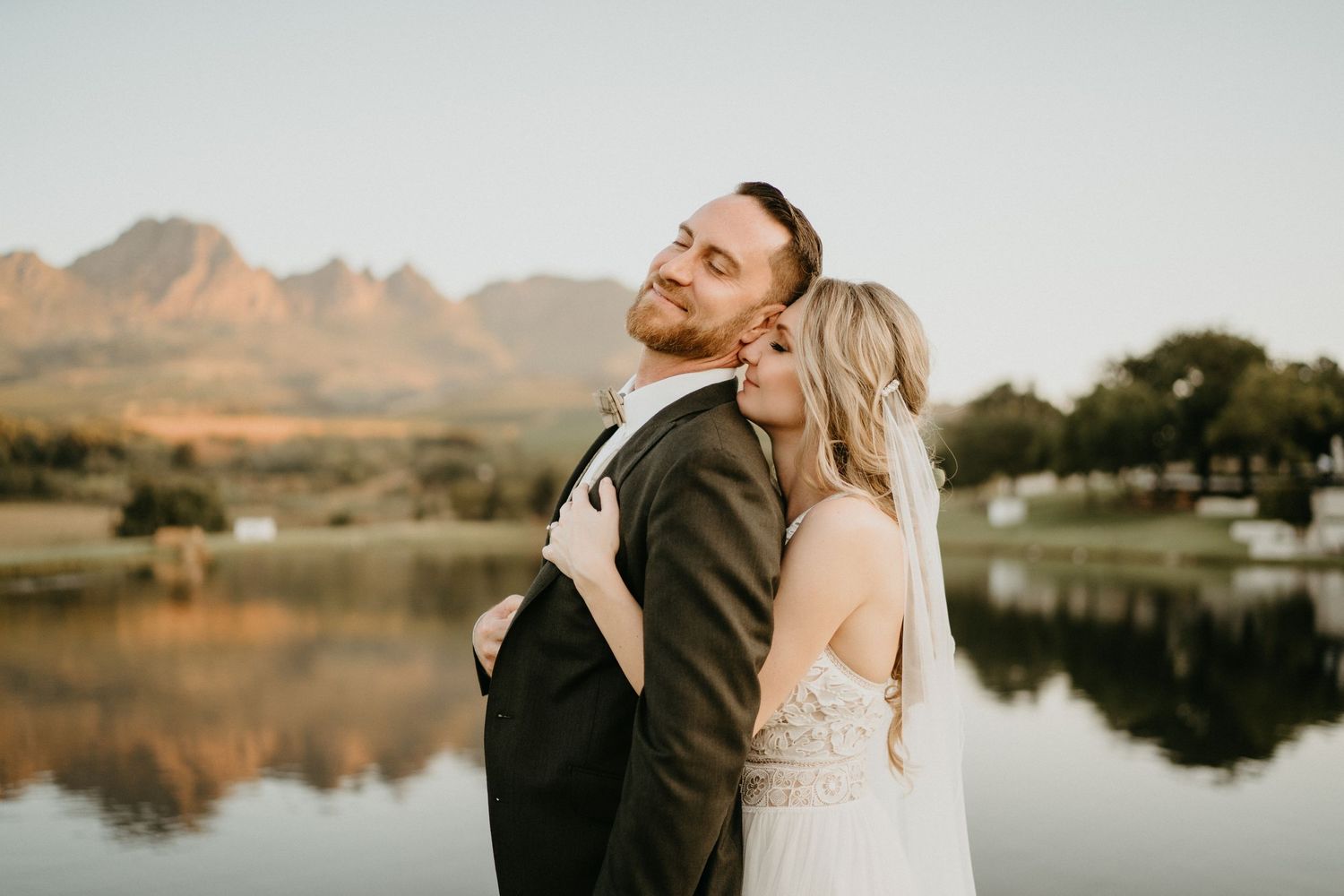 Romantic sunset portrait by mountain lake with couple in wedding attire.