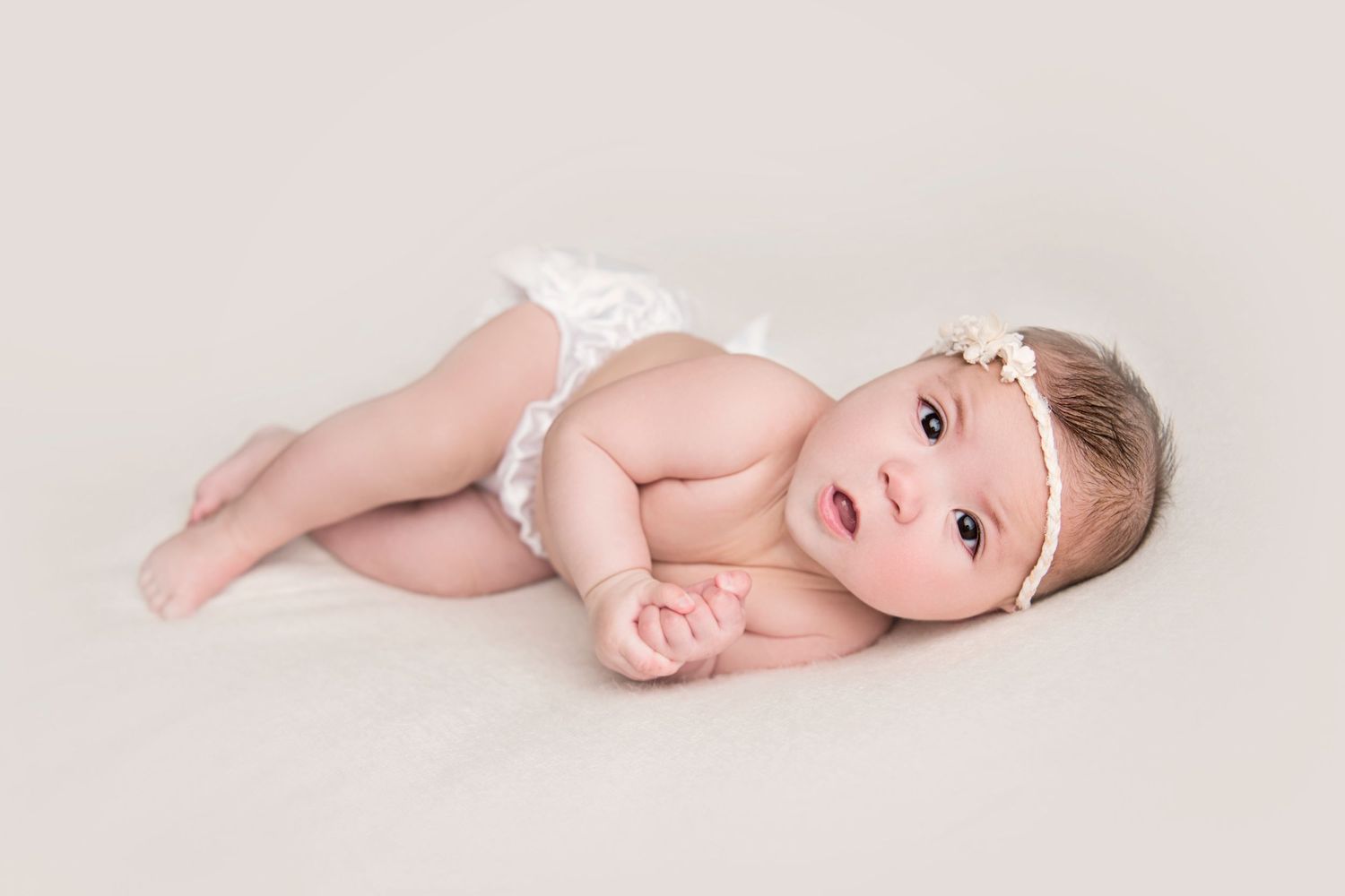 Baby wearing white headband lying on pink backdrop during professional portrait session.