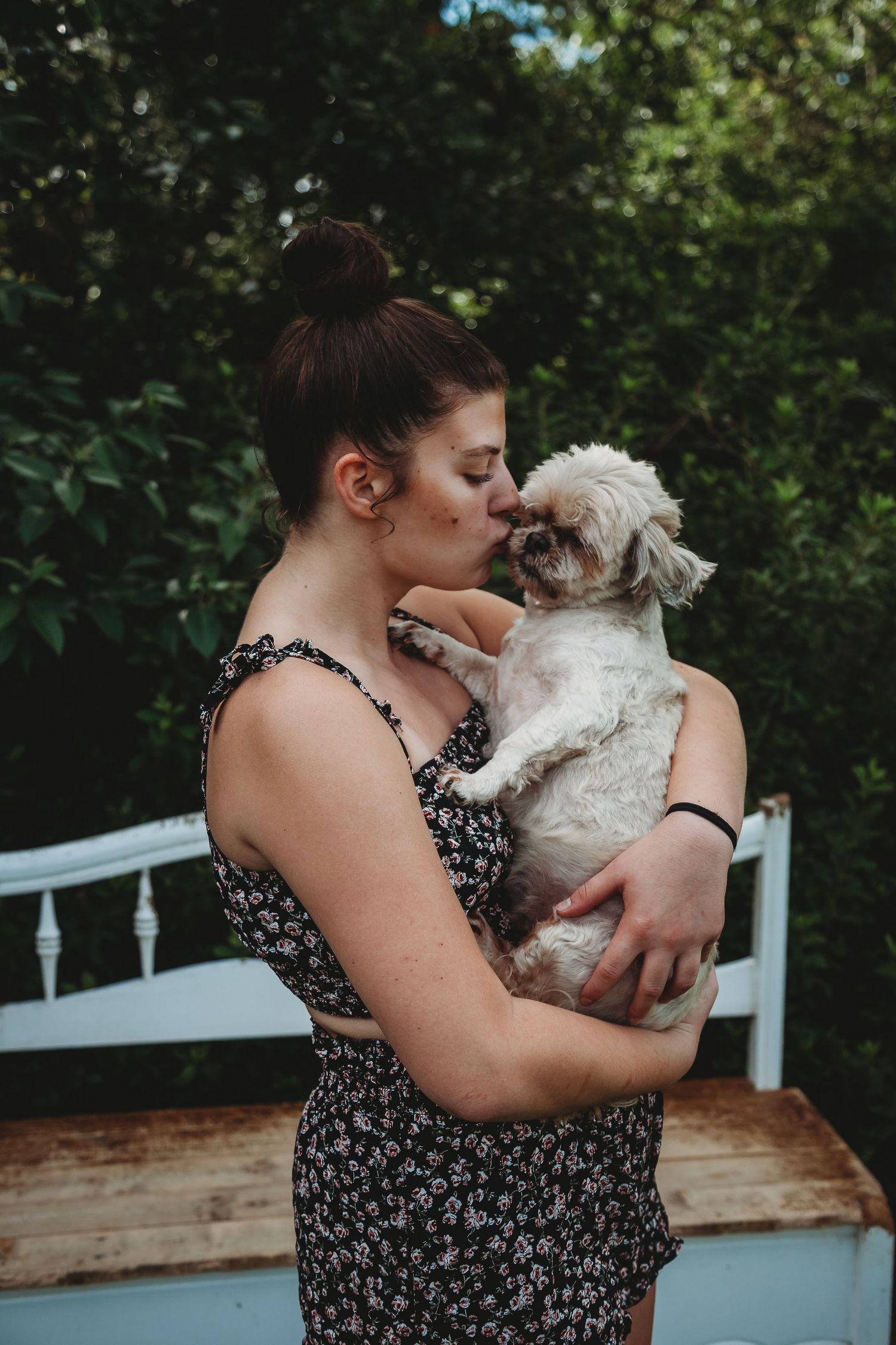 Small white dog being held and cuddled outdoors.
