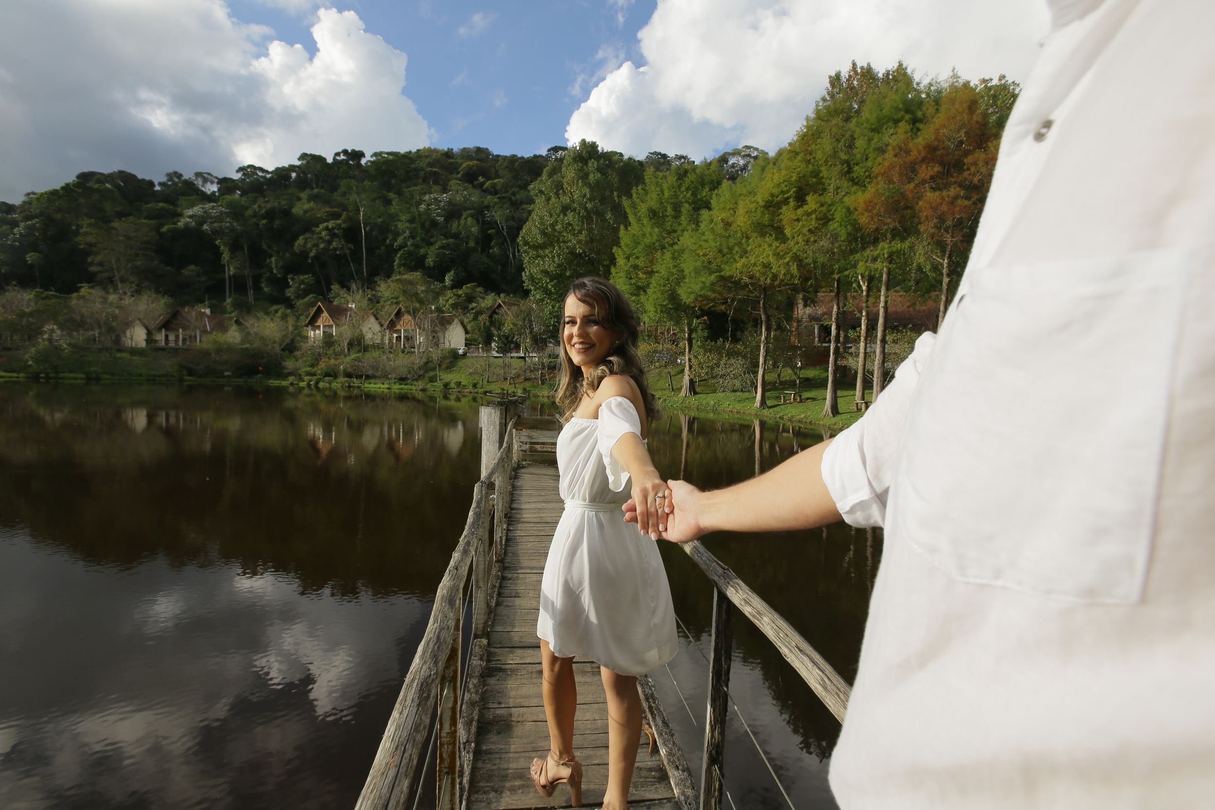 Couple poses together on a wooden dock overlooking a serene lake surrounded by trees.