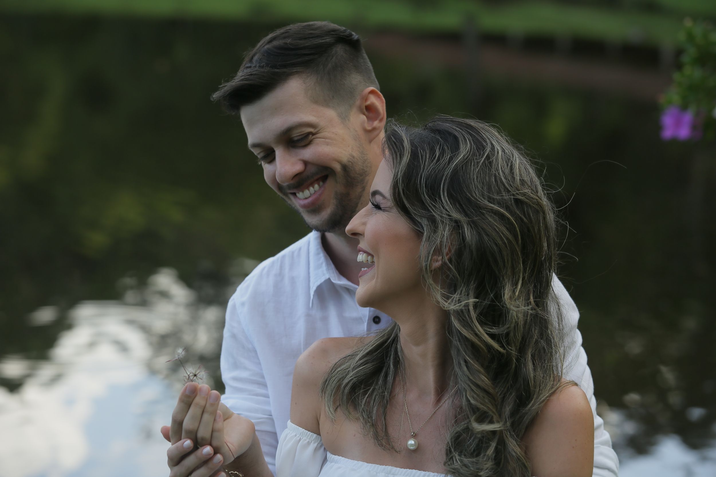 Intimate moment captured between couple by lakeside with natural scenery.