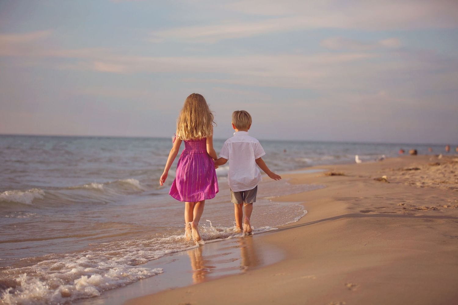 Two children walking together along beach shoreline at sunset.
