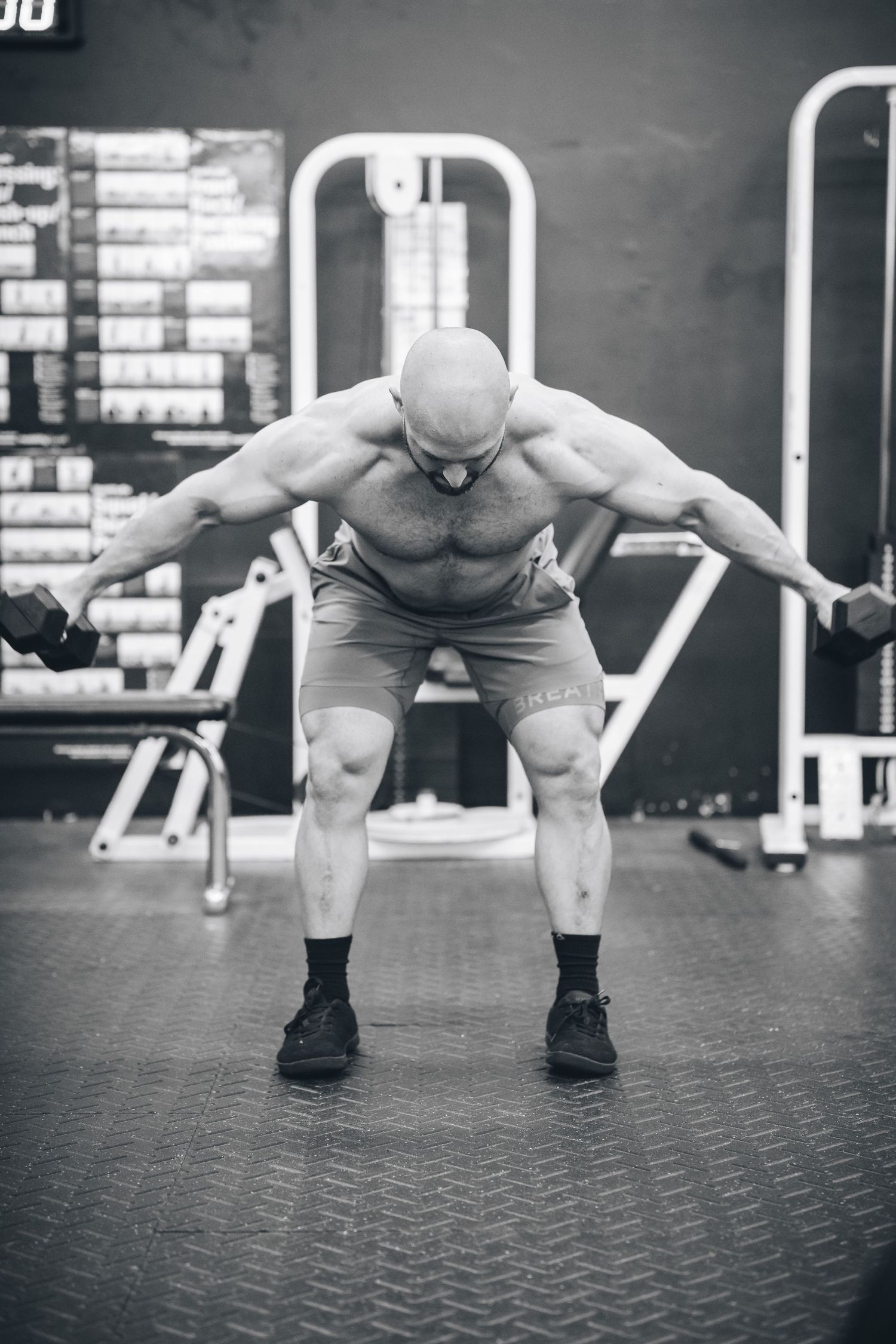 Muscular athlete performing a dumbbell workout in a black and white gym setting.