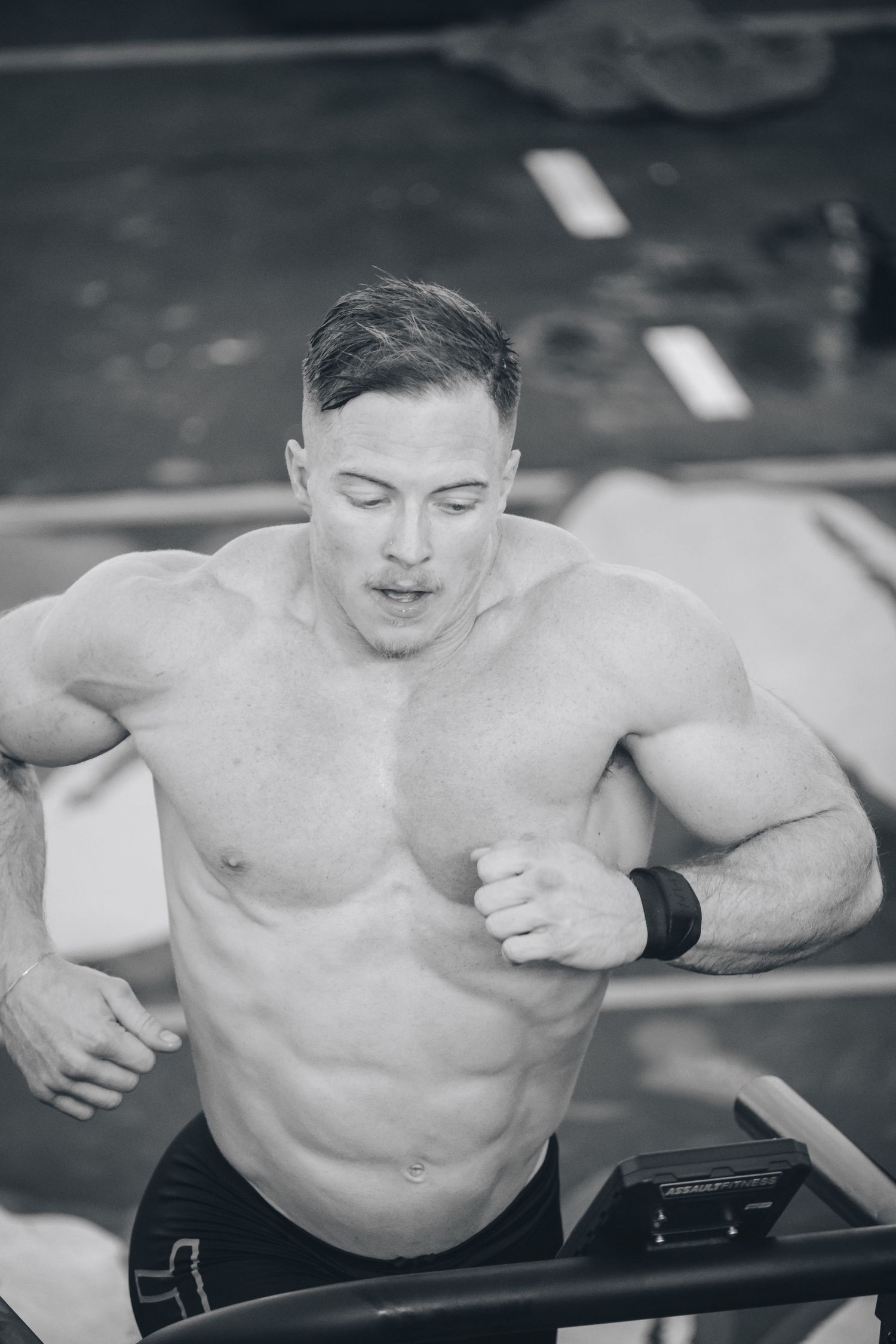 Shirtless athlete training intensely on exercise equipment in black and white photography.