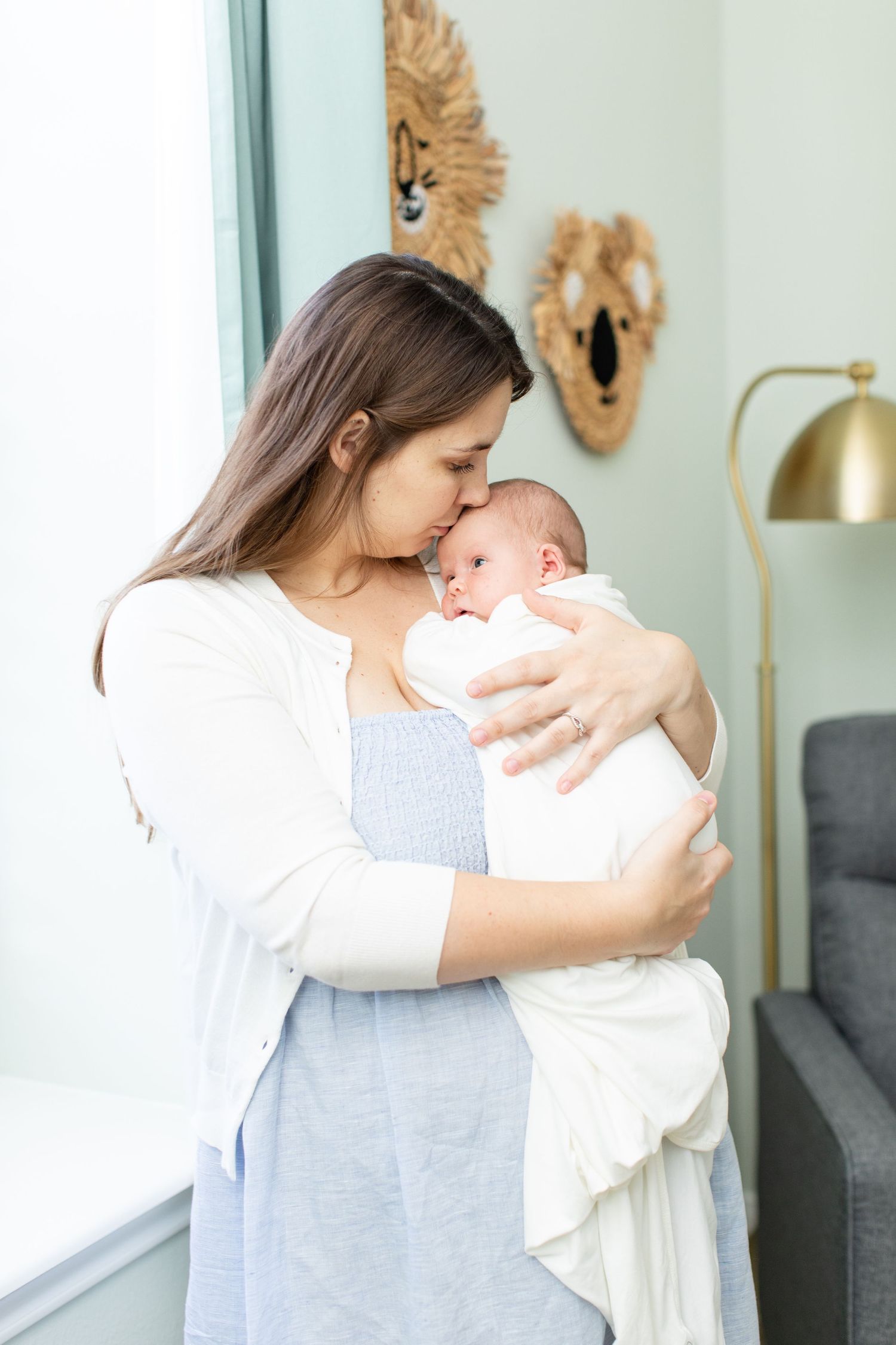 Woman in white and blue dress holding newborn baby near decorative wall art.